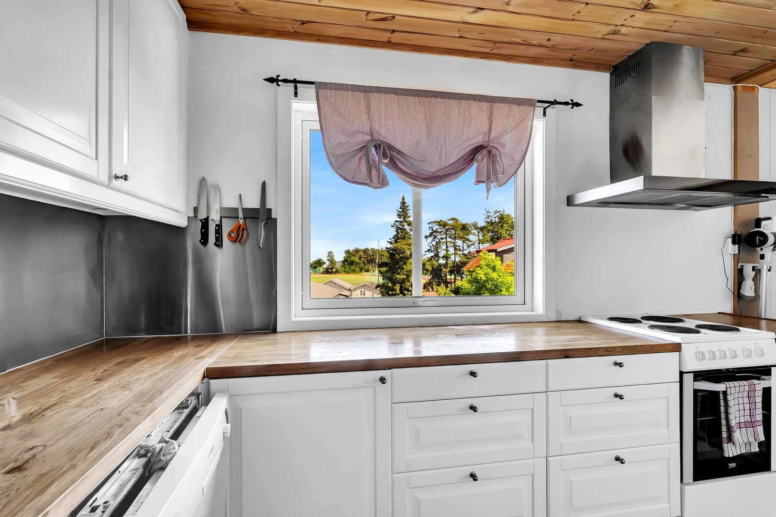 Kjøkkenet har innredning med hvite, profilerte fronter, heltre benkeplate og en moderne stålplate mellom benkeplate og overskap. Galleribilde