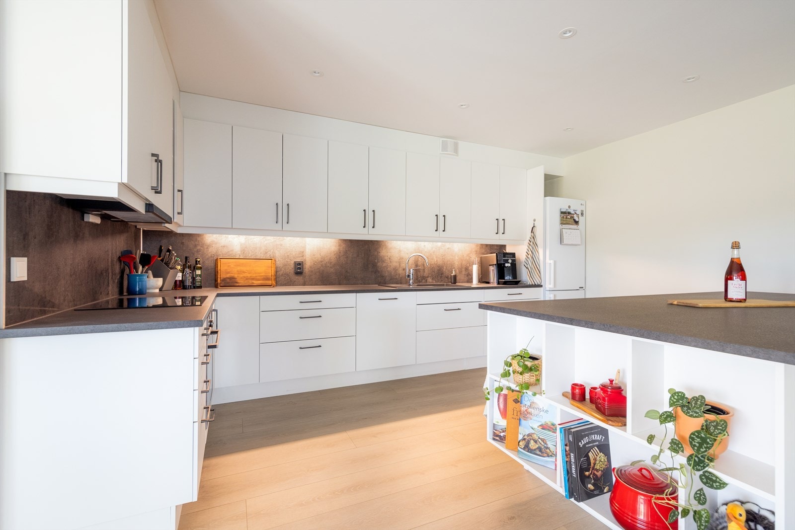 Innredningen har hvite, glatte fronter og er utstyrt med to integrerte stekeovner, integrert oppvaskmaskin og plass for frittstående kjøleskap. Galleribilde