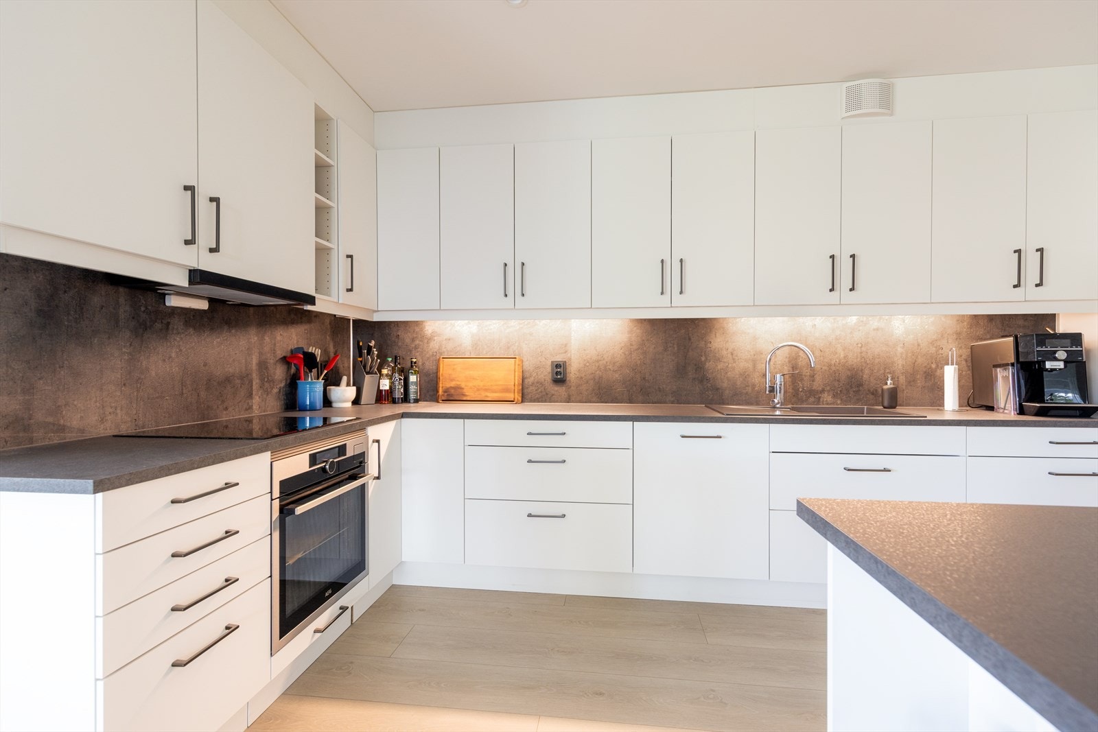 Videre er det nedfelt platetopp med kjøkkenventilator med kullfilter over, og en nedfelt oppvaskkum med avrenningsflate på siden. Galleribilde