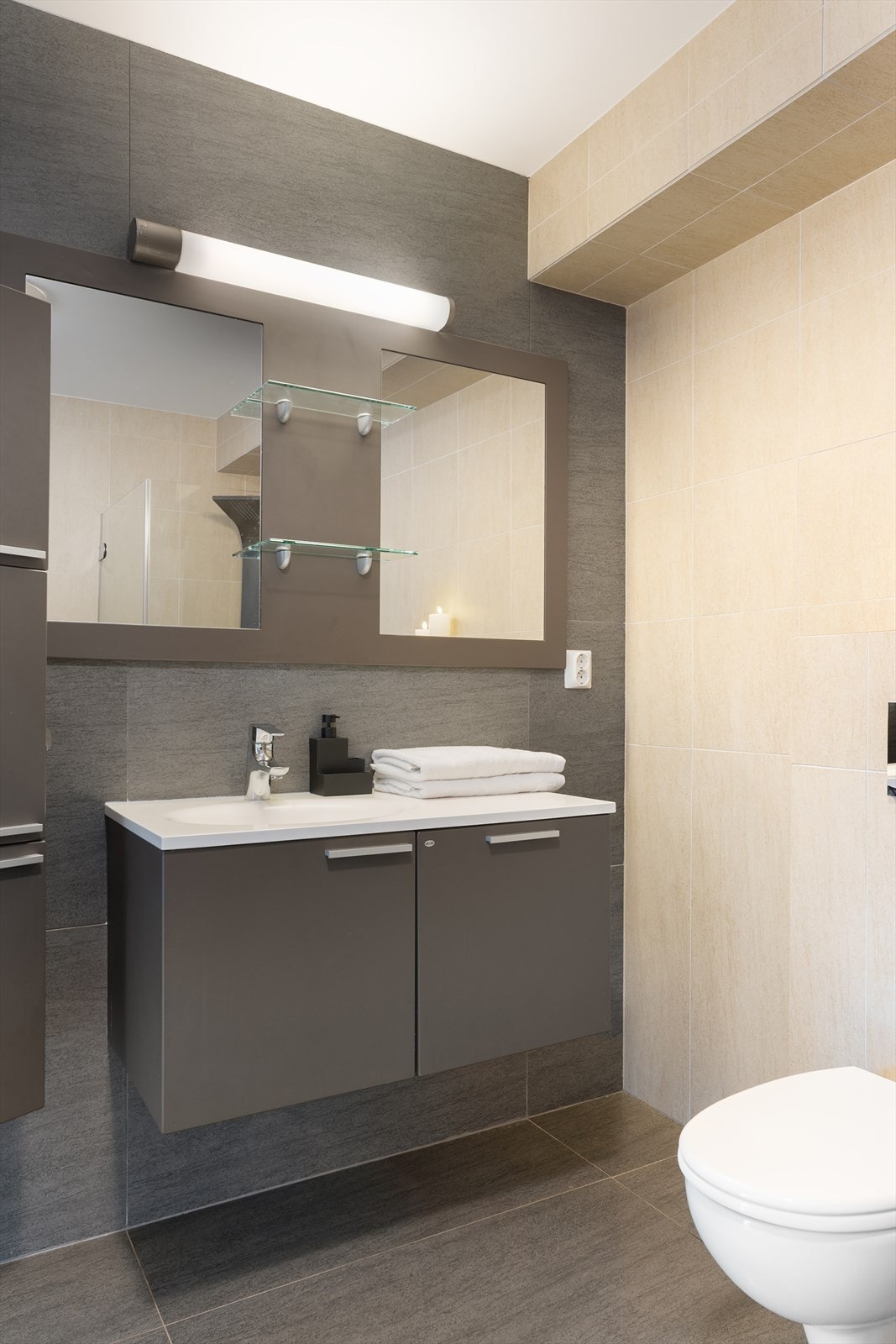 Badet er innredet med mørk baderomsinnredning, vegghengt toalett og dusjnisje med glassdører - det er også opplegg for vaskemaskin Galleribilde