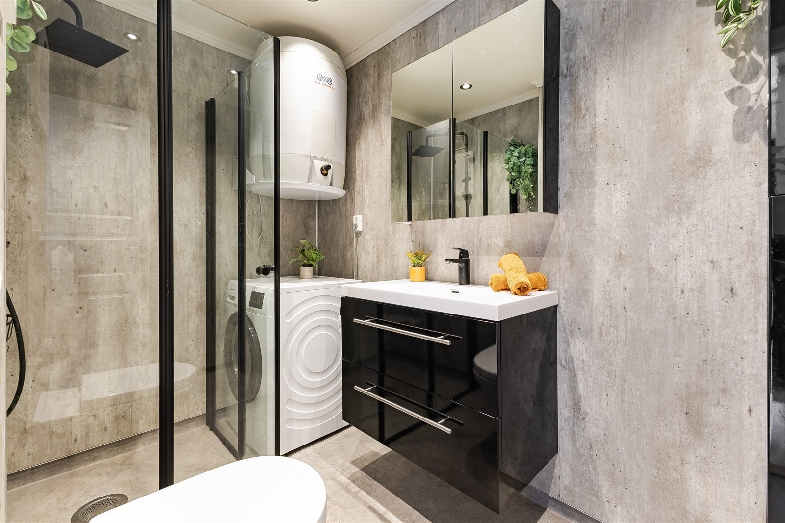 Rommet har servant, veggmontert toalett, dusjvegger/hjørne og opplegg for vaskemaskin. Galleribilde