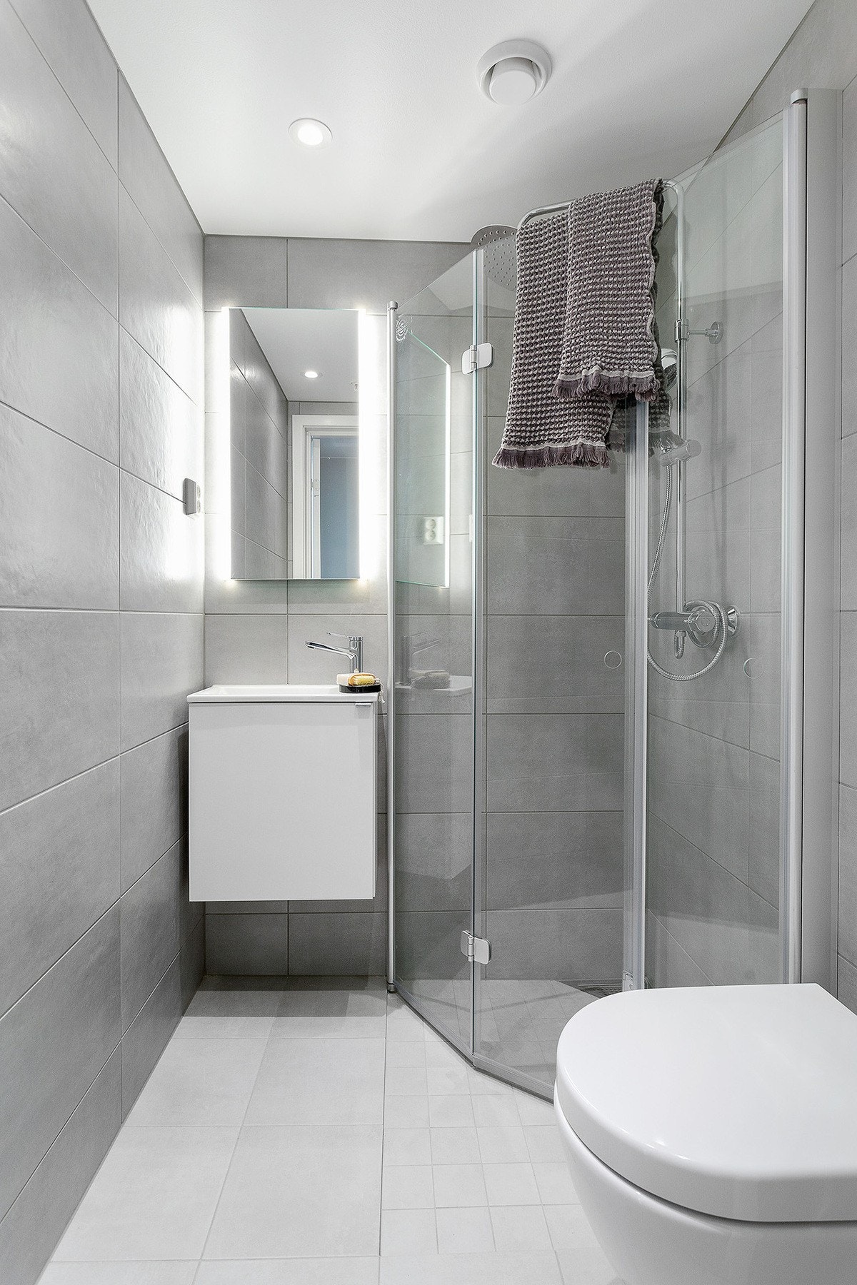 Leilighetens andre bad med flislagte overflater, dusjhjørne og vegghengt toalett og skap Galleribilde