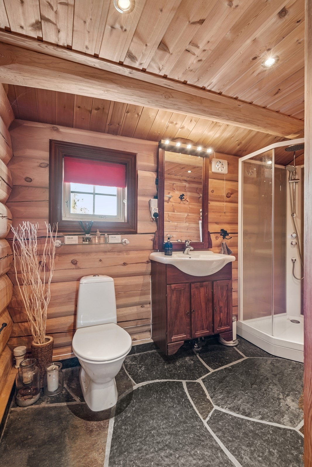 Pent baderom med skifer på gulv, tømmervegger og panel med downlighst i himling. Galleribilde