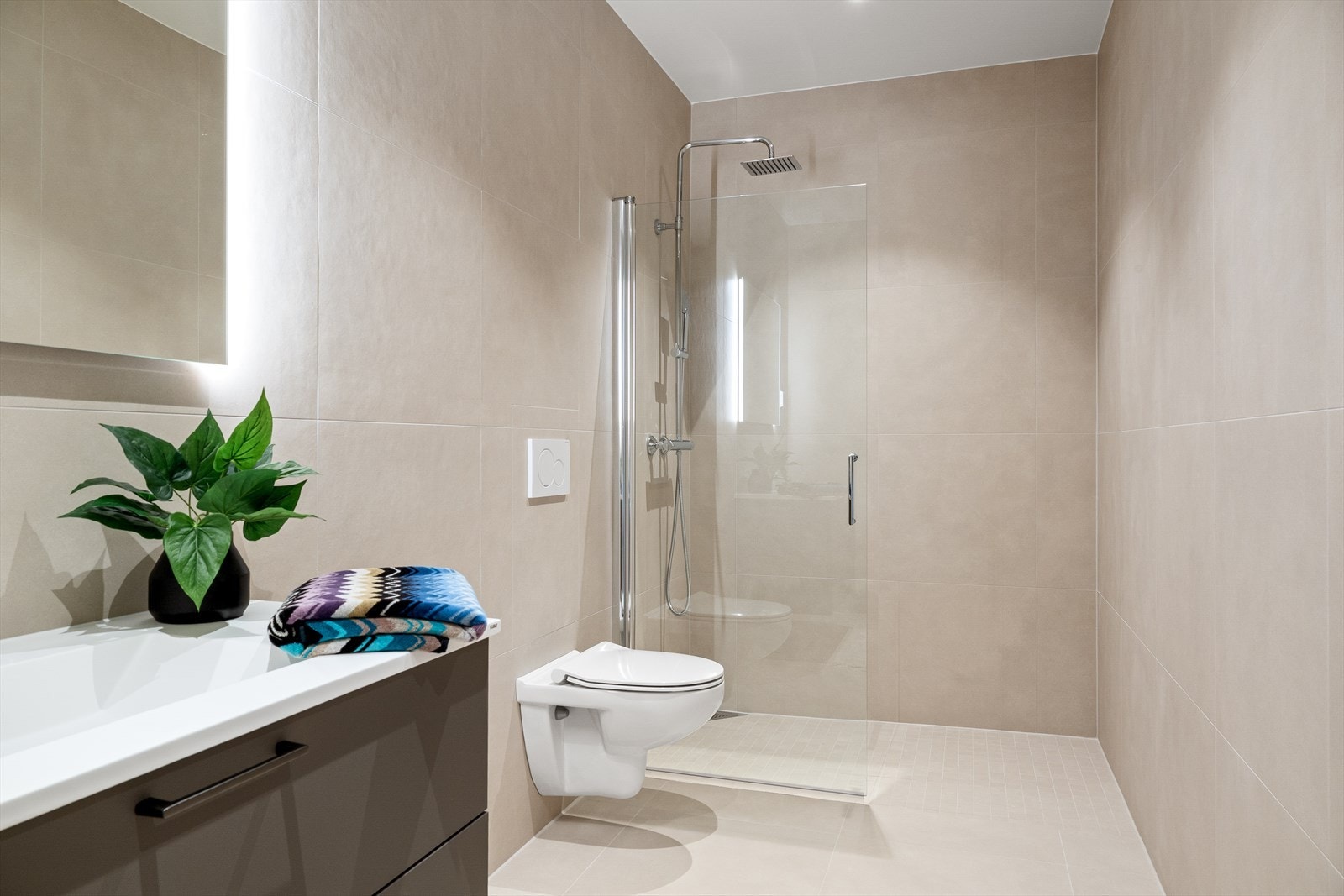 Det er vannbåren varme i gulv. Badet er innredet med vegghengt toalett, vask i seksjon, speil med belysning og dusjhjørne. Galleribilde