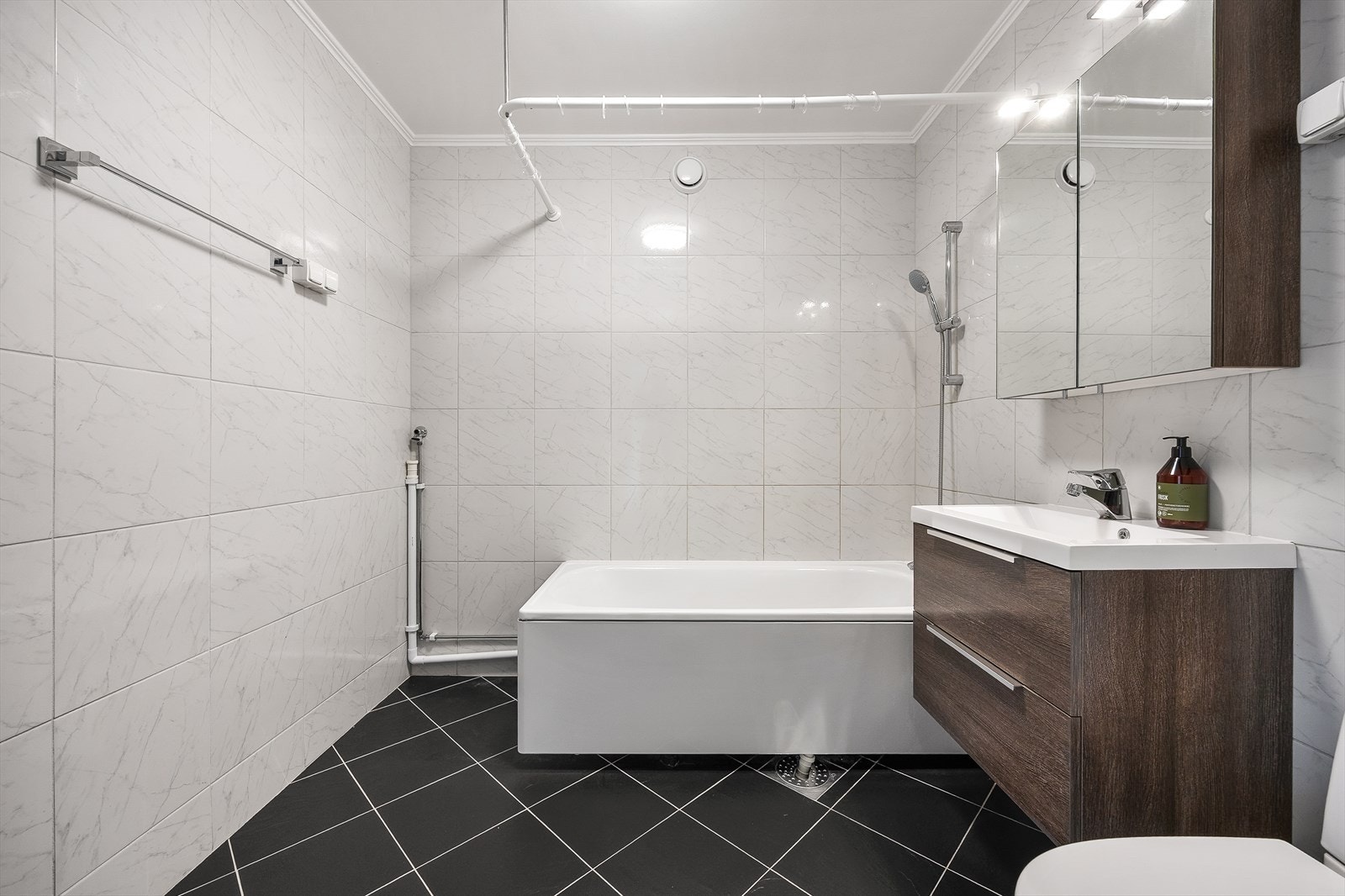 Badet er utstyrt med badekar med dusj og forheng, gulvstående wc og servantinnredning med skuffer og overskap Galleribilde
