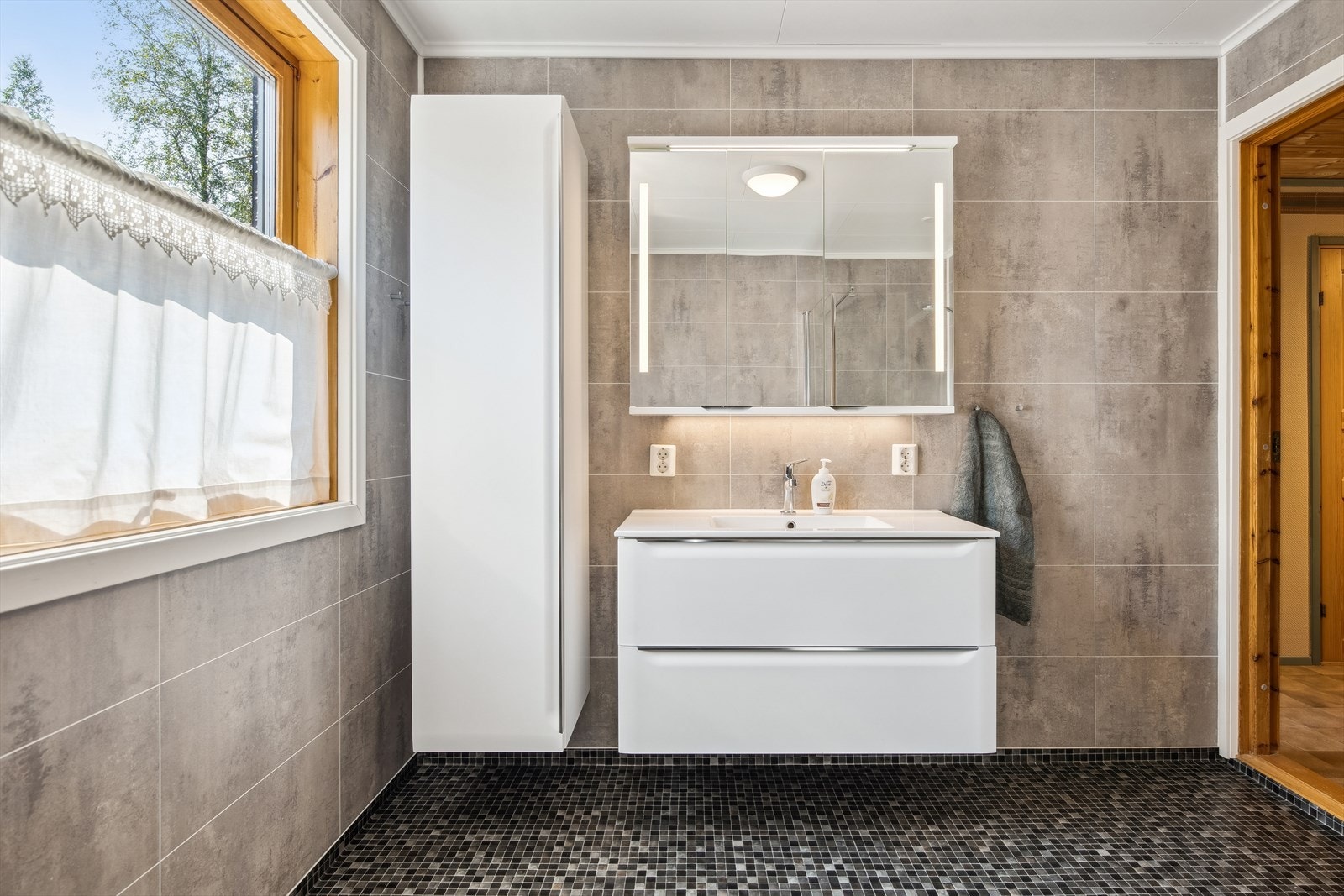 På badet er det heldekkende servant i skuffeinnredning, speil med lys, høyskap og det er montert stikkontakter for hårføner m.m. Galleribilde