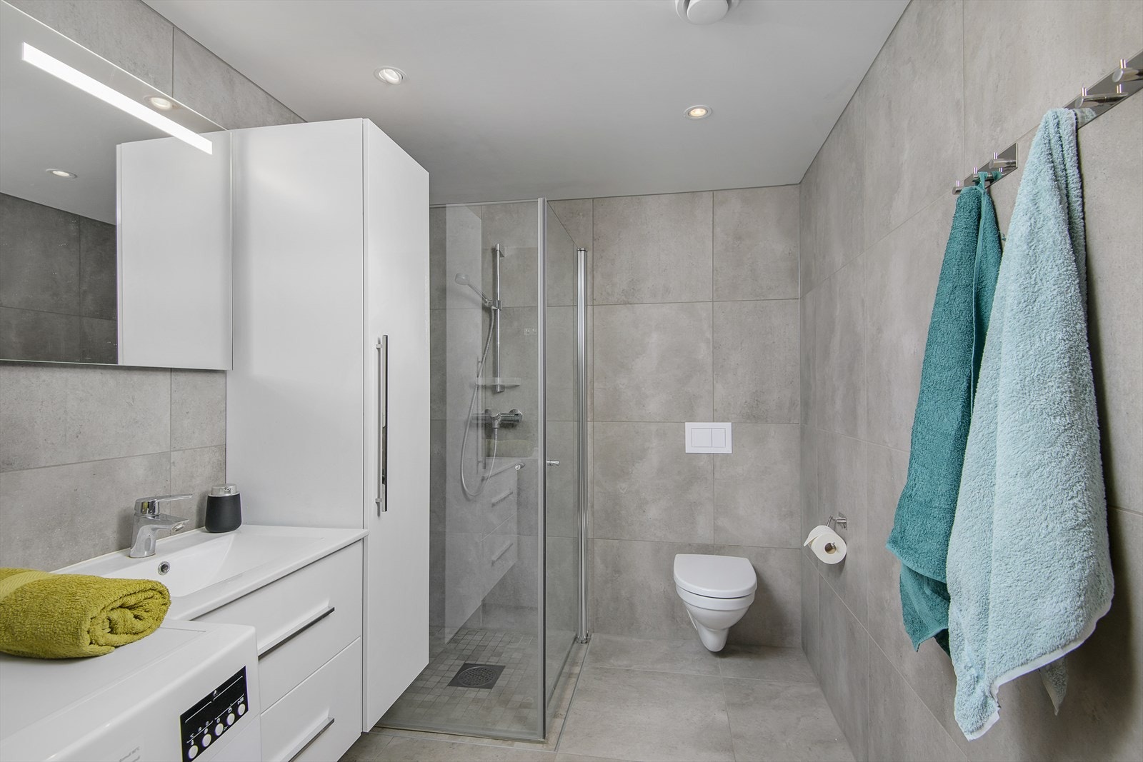 Flislagt bad med hvit baderomsinnredning. Vegghengt toalett og dusjdører i herdet glass. Innfelte downlights i himling. Galleribilde