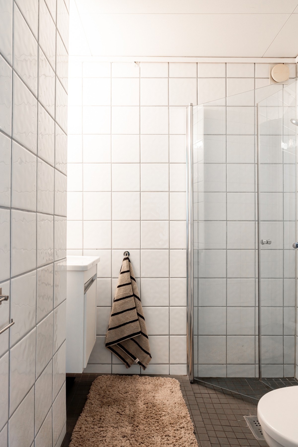 Pent baderom med hvite fliser på vegg og grå fliser på gulv med varmekabler i gulvstøp. Galleribilde