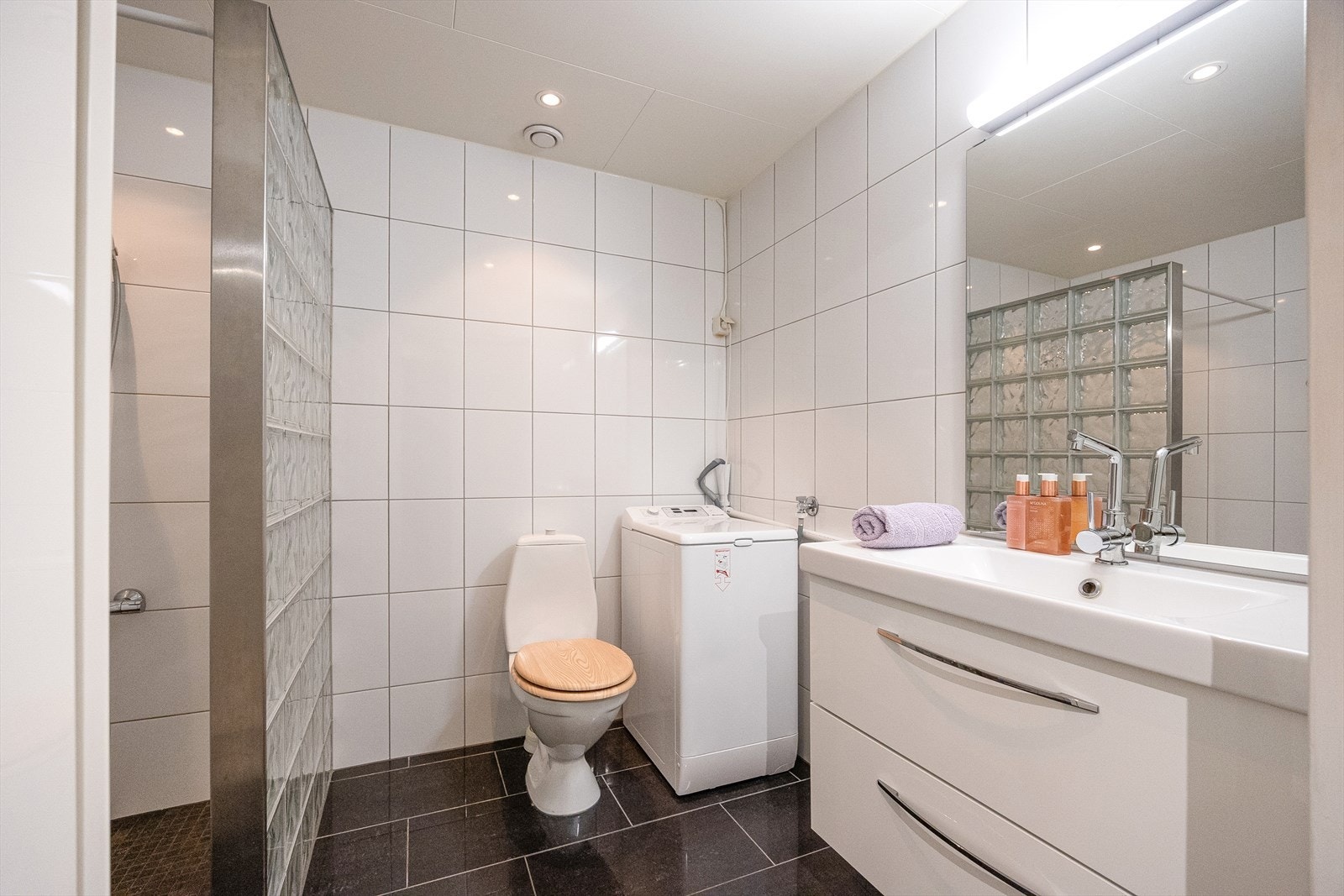 Badet er helfliset i tidløse farger og er innredet med servant med underskap, speil, dusjhjørne, WC, samt opplegg for vaskemaskin. Galleribilde