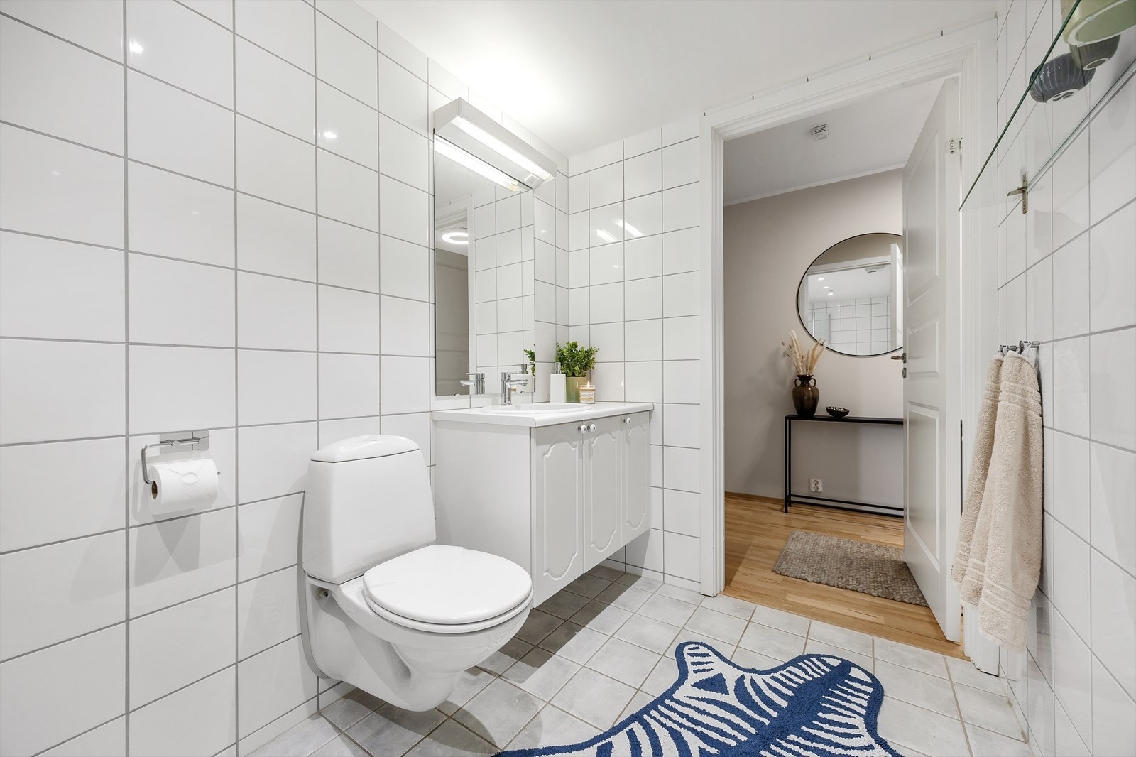 Badet er innredet med servant i baderomsinnredning, speil, vegghengt toalett, dusjhjørne med innfellbare glassvegger og opplegg for vaskemaskin. Galleribilde