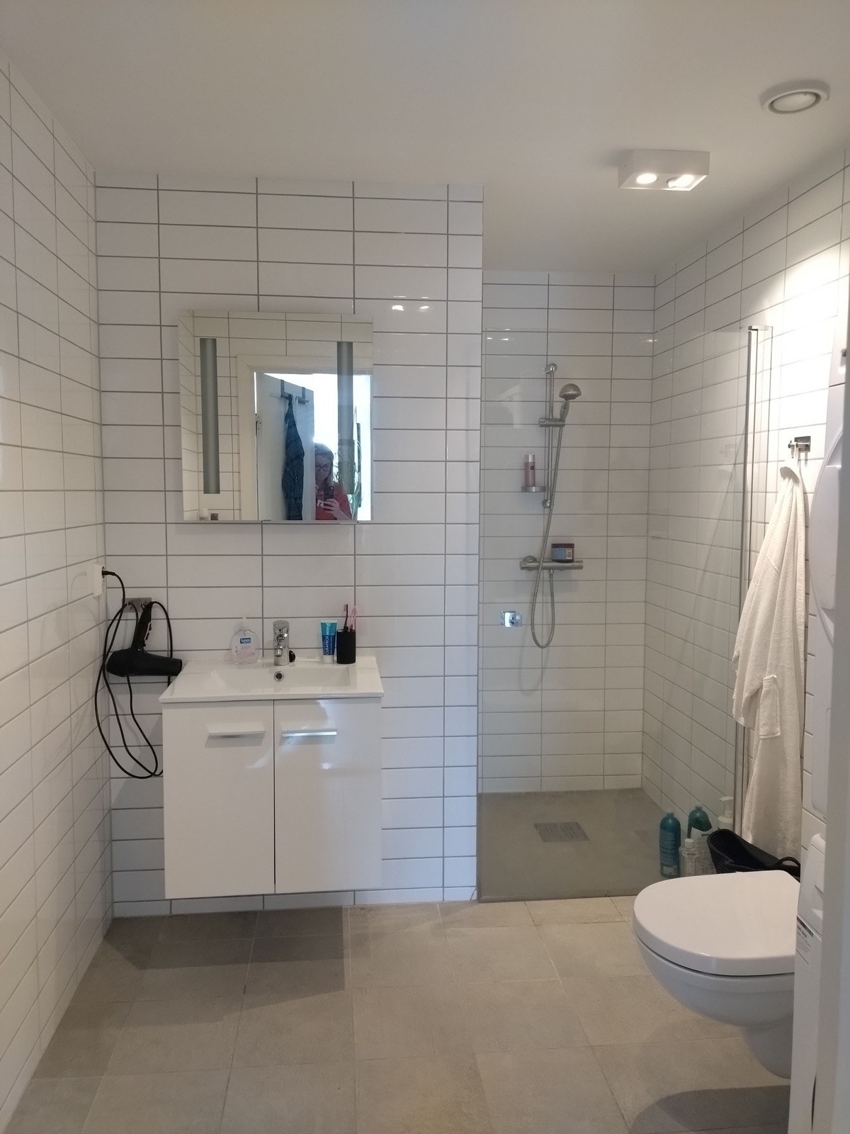 Pent flislagt bad med vegghengt toalett, dusj og servant m/innredning. Galleribilde