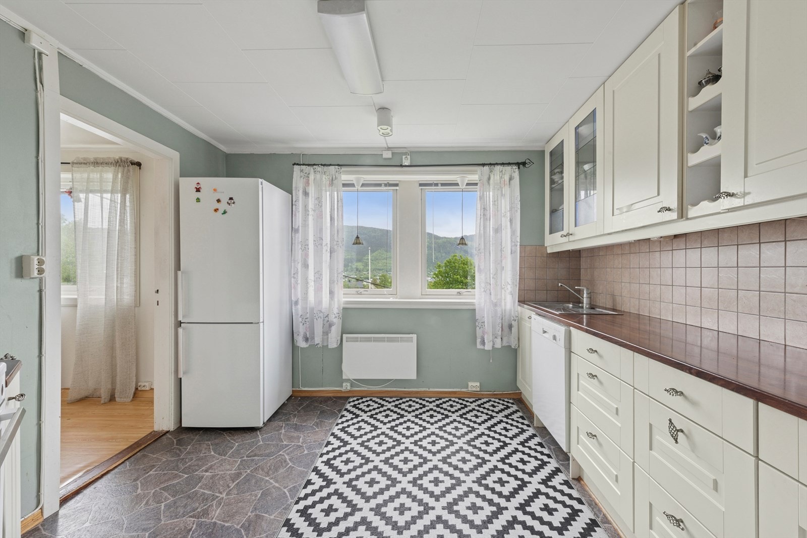 Kjøkkenet er delvis atskilt fra stuen og har hvite profilerte fronter og framstår som romslig (L1) Galleribilde