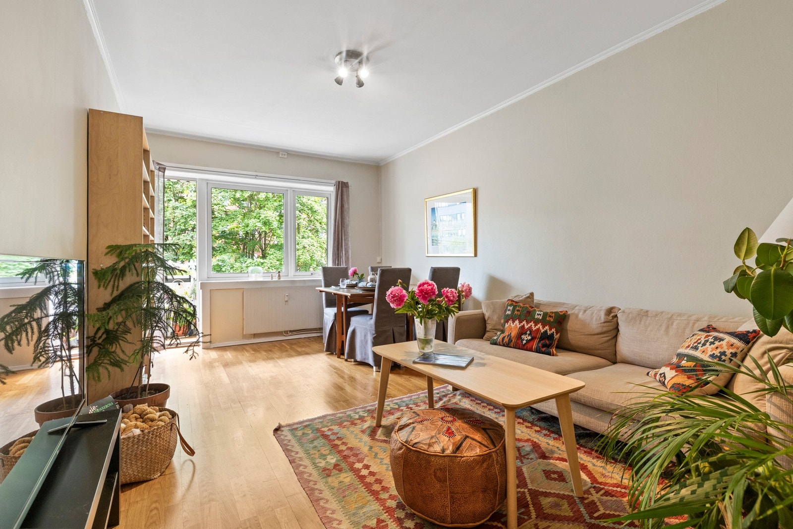 En lys og romslig stue med både spiseplass og sofagruppe, perfekt for sosiale sammenkomster. Store vinduer slipper inn rikelig med lys og gir utsikt til grønne omgivelser Galleribilde