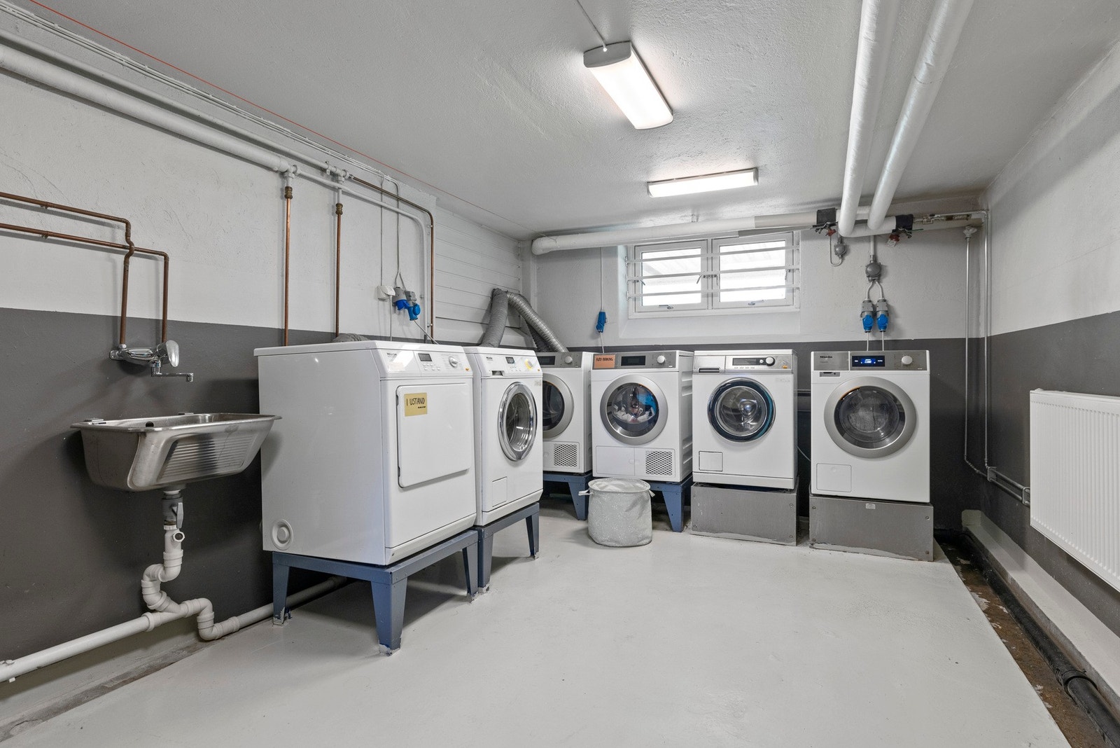 Felles vaskerom i bygningen, utstyrt med flere moderne vaskemaskiner og tørketromler. Et praktisk og effektivt tilbud for beboerne Galleribilde
