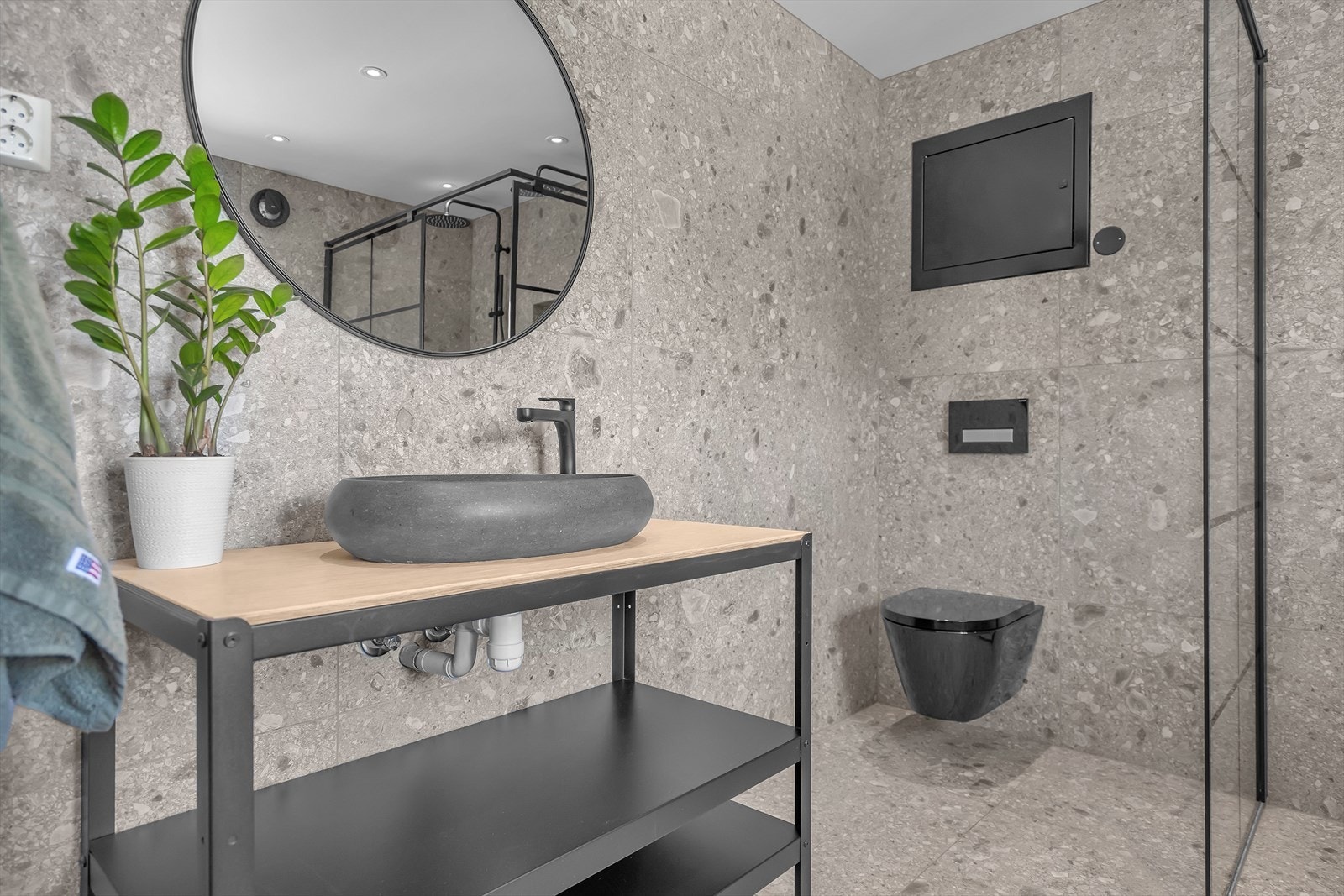 Badet har vegghengt toalett, innredning med skålvask og hyller, dusjnisje med glassvegger og opplegg til vaskemaskin/tørketrommel Galleribilde