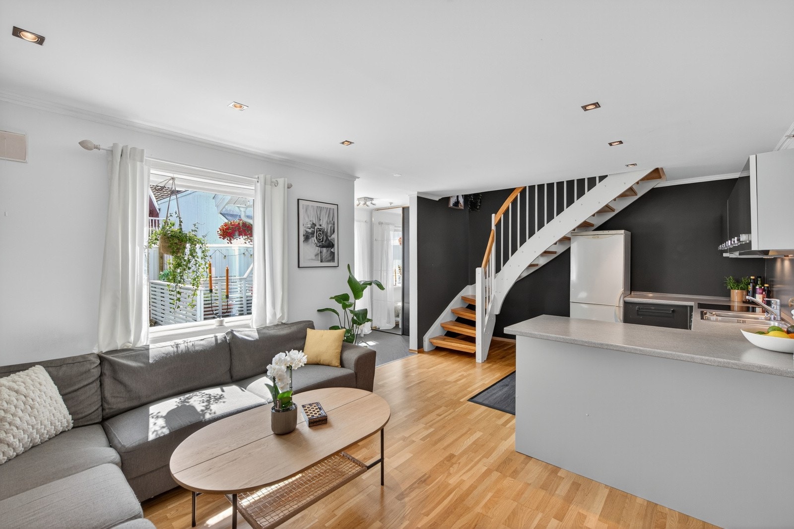 Her får du stue og kjøkken i en åpen løsning, med kontrastvegg som harmonerer elegant med det ellers lyse rommet. Downlights og store vindusflater sørger for å lyse opp rommet Galleribilde