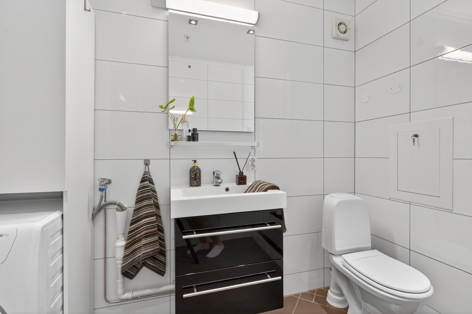Badet er innredning med dusjkabinett, opplegg til vaskemaskin, toalett og servant i innredning med skuffer Galleribilde
