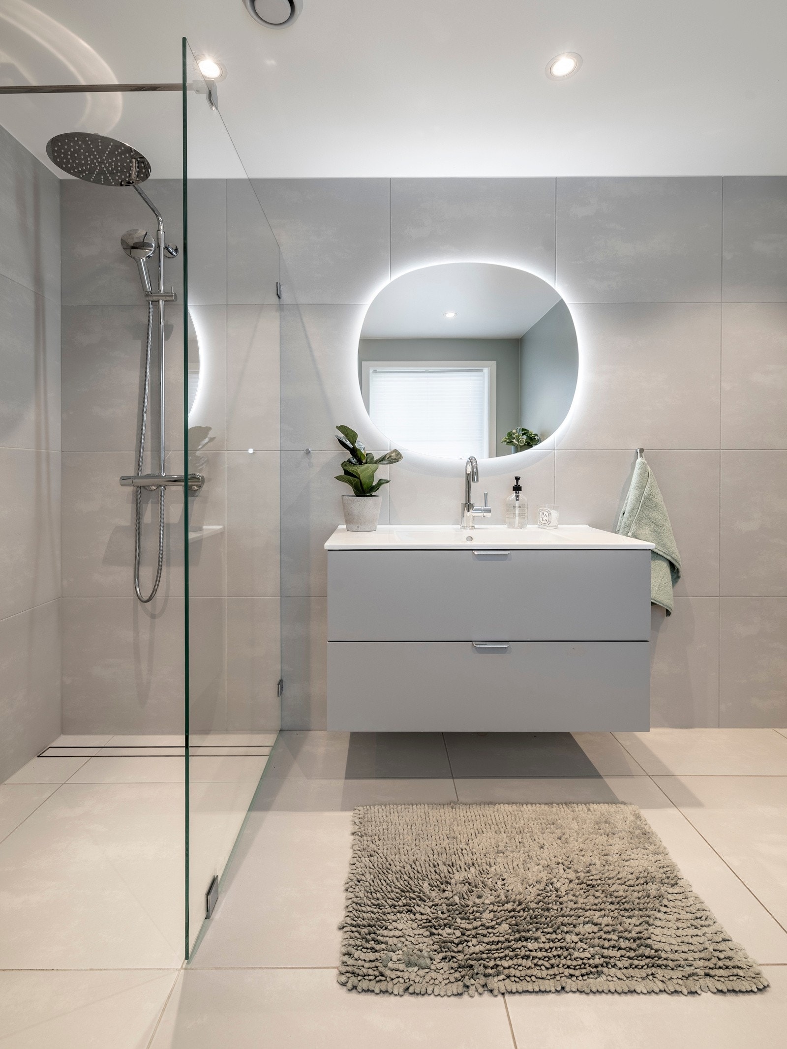 Badet er innredet med servantinnredning, speil med lys på vegg over servant, vegghengt toalett og dusjhjørne med en glassvegg. Galleribilde
