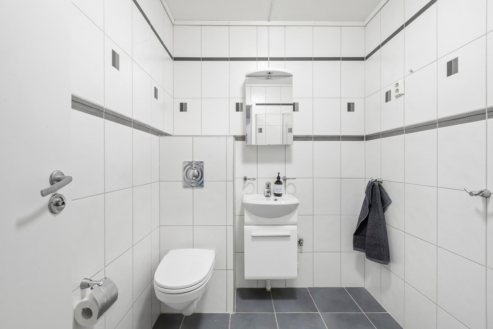 Flislagt bad med servant, speilskap og vegghengt toalett. Galleribilde