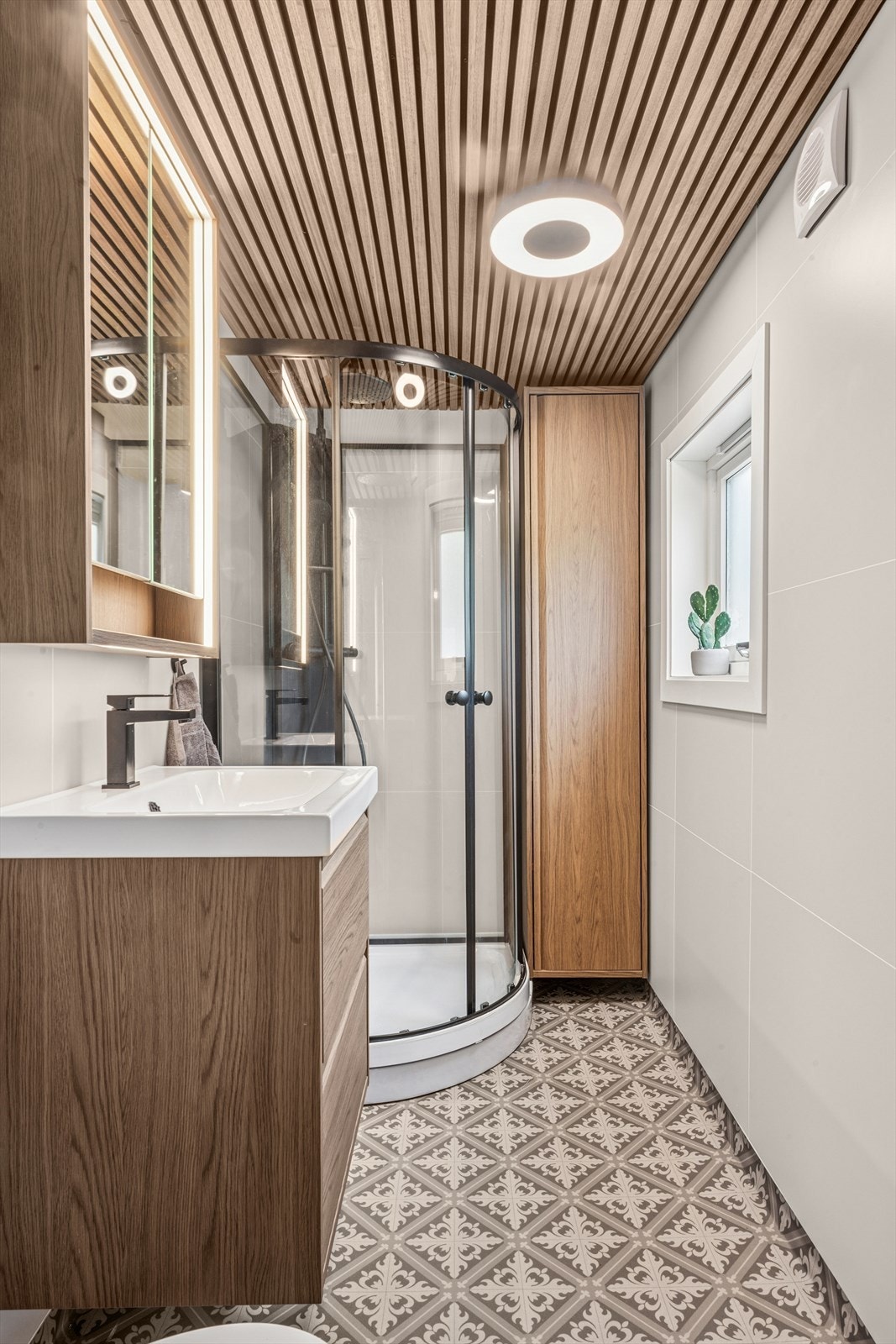 Det er utstyrt med servant, gulvmontert toalett, dusjkabinett og speilskap med belysning. Galleribilde