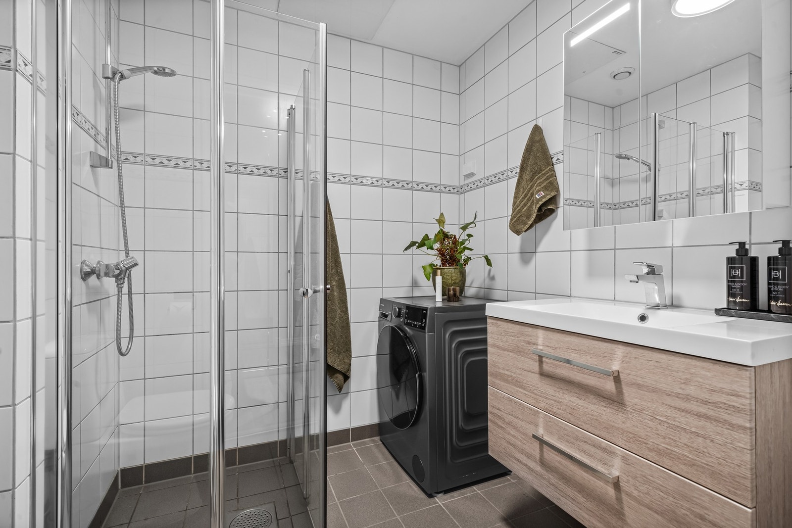 Badet er innredet med frittstående toalett, svingbare dusjdører i glass, servant med underskap og speil. Galleribilde