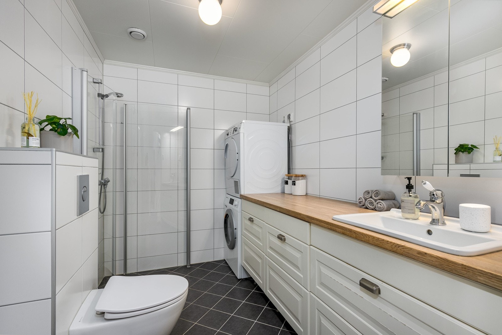 Flislagt bad- og kombinert vaskerom i boligens 2. etasje, nytt i 2011. Innredningen består av profilert servantmøblement med topp-plate i heltre eik, rikelig med skuffer og nedfelt vaskekum i porselen. Videre har badet speil, toalett, samt dusjhørne. Galleribilde