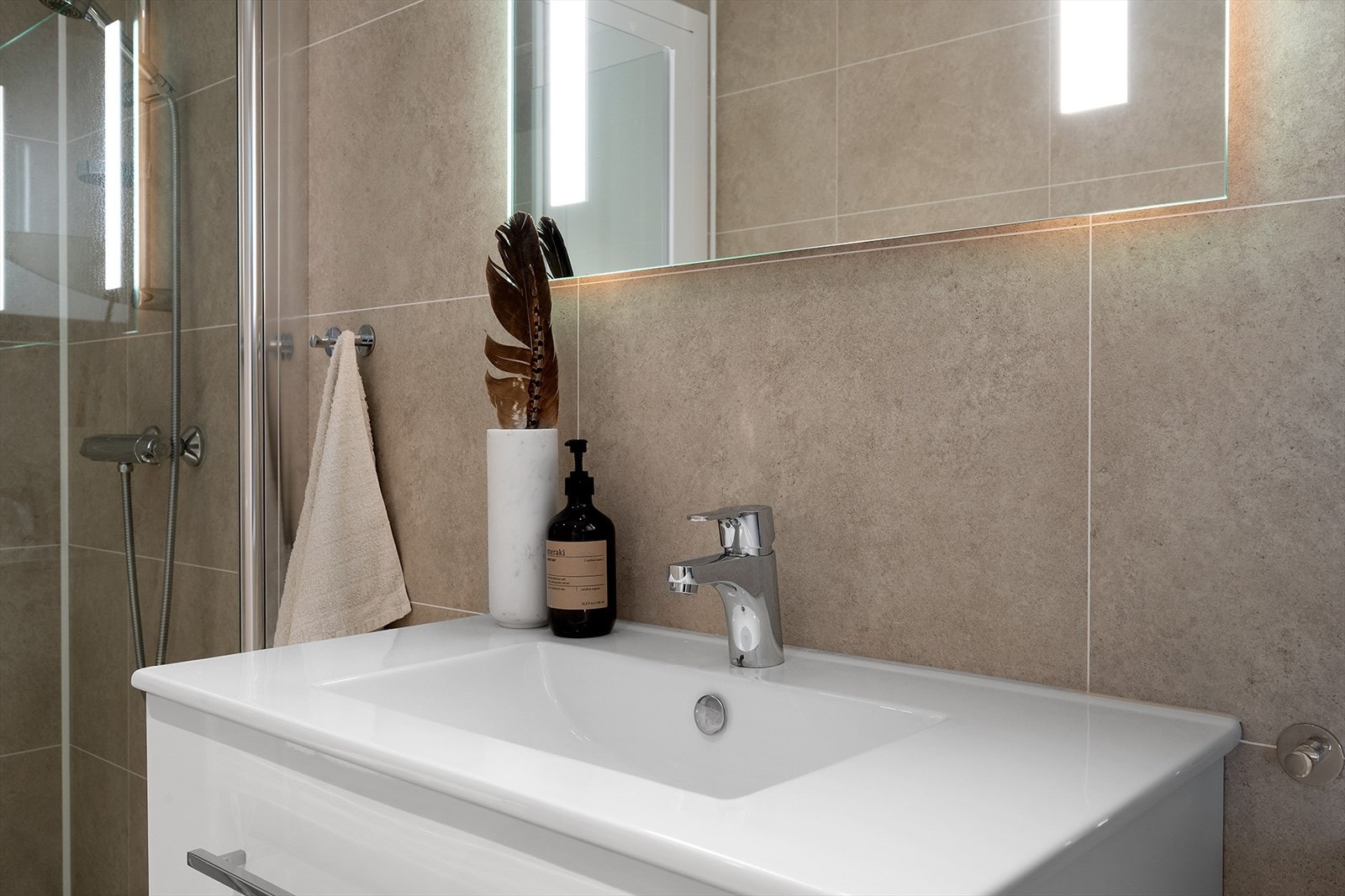 Badet er innredet med dusjvegger, dusjbatteri, veggfestet WC og baderomsinnredning med speil og heldekkende servant. Galleribilde