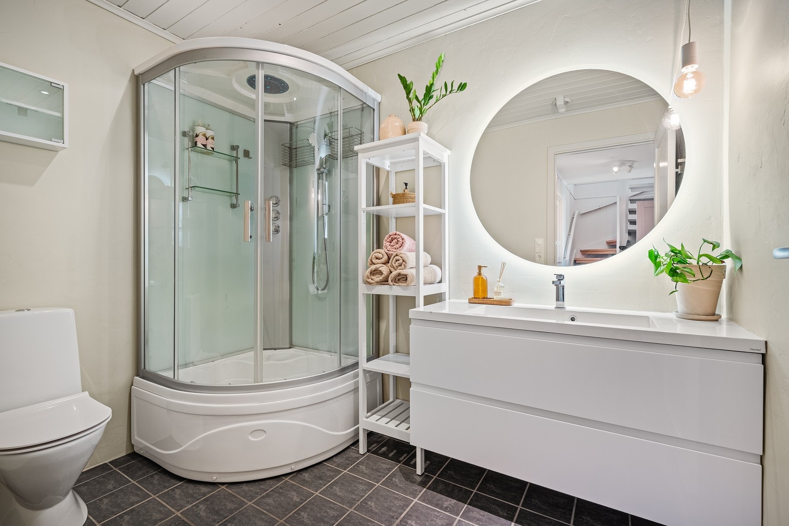 Badet er utstyrt med dusjkabinett med kar, toalett, servant med skuffeinnredning og speil med lys. Galleribilde