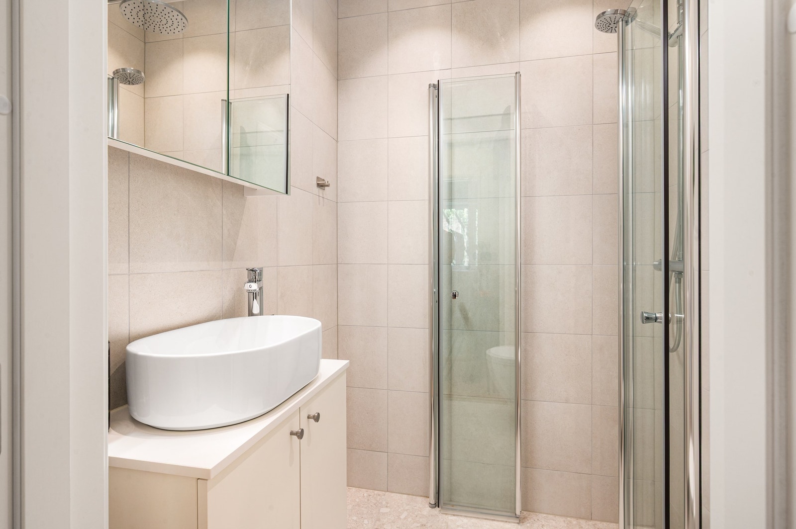 Badet er innredet med vegghengt klosett, servant nedfelt i innredning, speilskap og dusjhjørne med svingbare glassdører. Varmekabler i gulv. Galleribilde