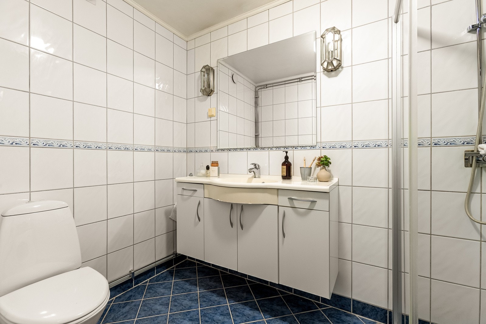 Badet er helfliset med hvit servantinnredning, speil, toalett og dusjhjørne med skyvedører. Galleribilde