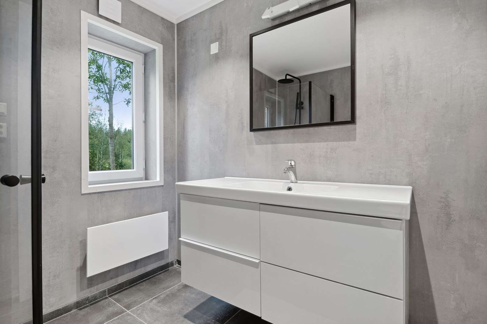 Badet er utstyrt med innfellbare dusjdører, veggmontert wc, servantskap og naturlig avtrekk. Opplegg til vaskemaskin. Galleribilde