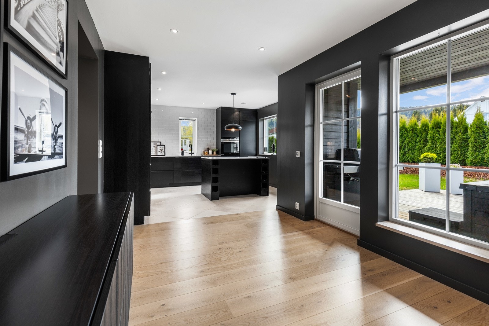 Moderne kjøkken med mørke fronter og lys parkett. Store vinduer gir mye naturlig lys og utsikt til hagen. Galleribilde