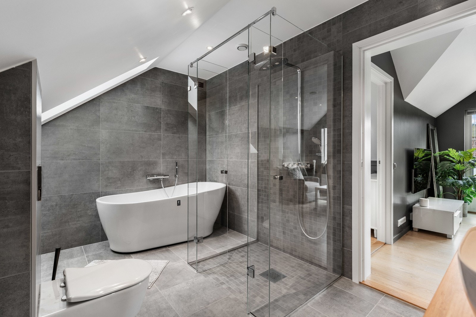 Moderne bad med frittstående badekar, dusjhjørne med glassvegger og store grå fliser. Galleribilde