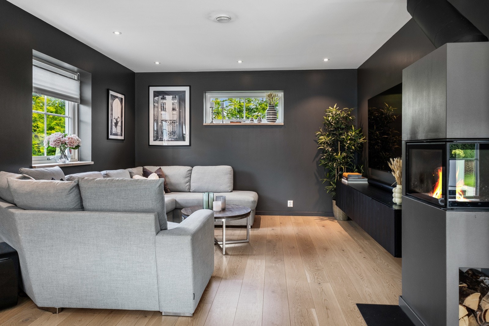 Stue med peis, plass til sofa, mørke vegger og stort vindu. Lys parkettgulv gir en lun atmosfære. Galleribilde