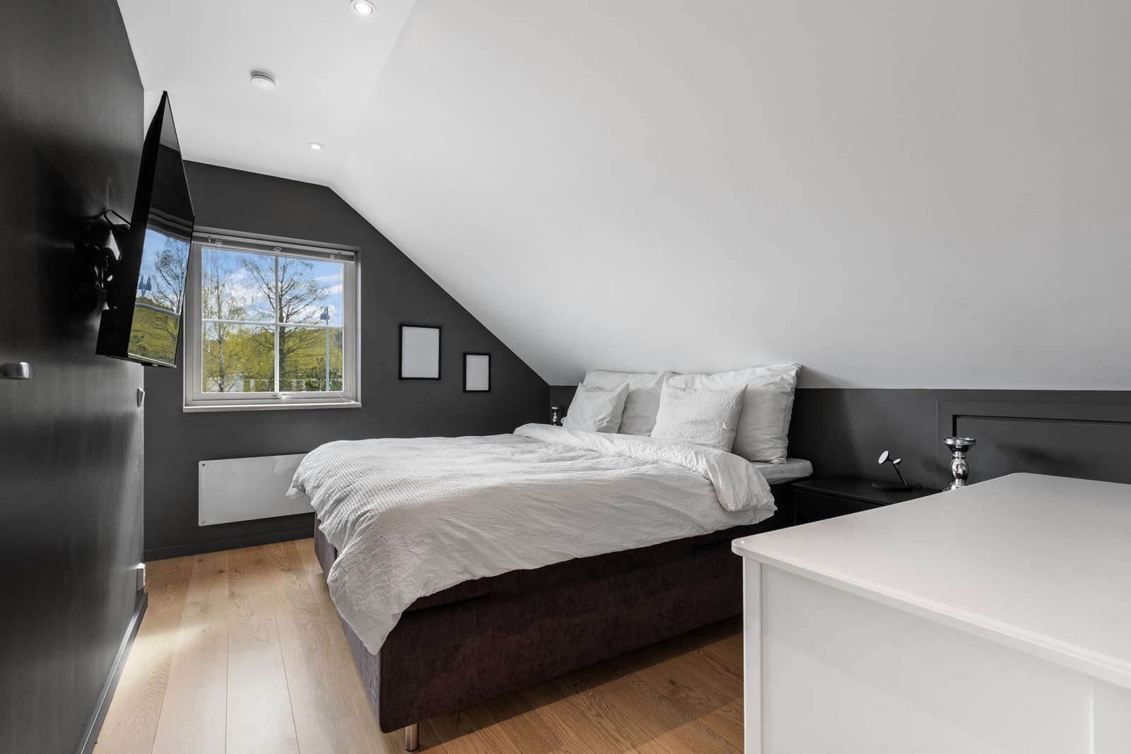 Soverom med skråtak, vindu med utsikt, veggmontert TV og dobbeltseng. Galleribilde