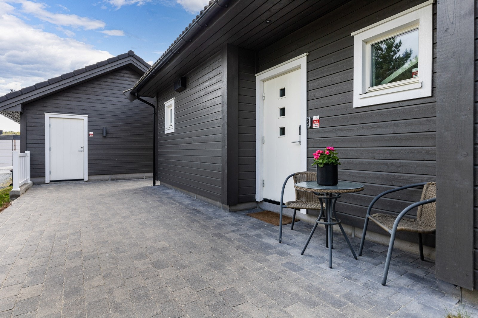 Moderne inngangsparti med grå fasade, hvit dør og brosteinsbelagt uteplass. Galleribilde