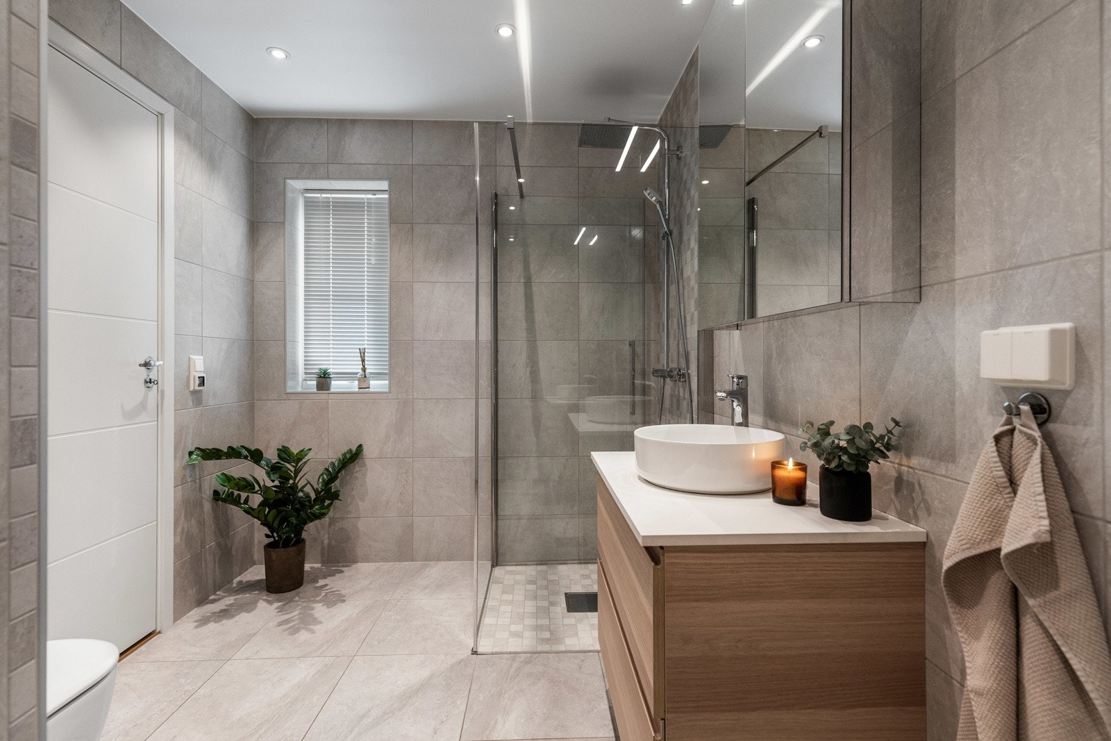 Moderne bad med dusjhjørne, vegghengt toalett og servant på skap. Fliser på gulv og vegger. Galleribilde