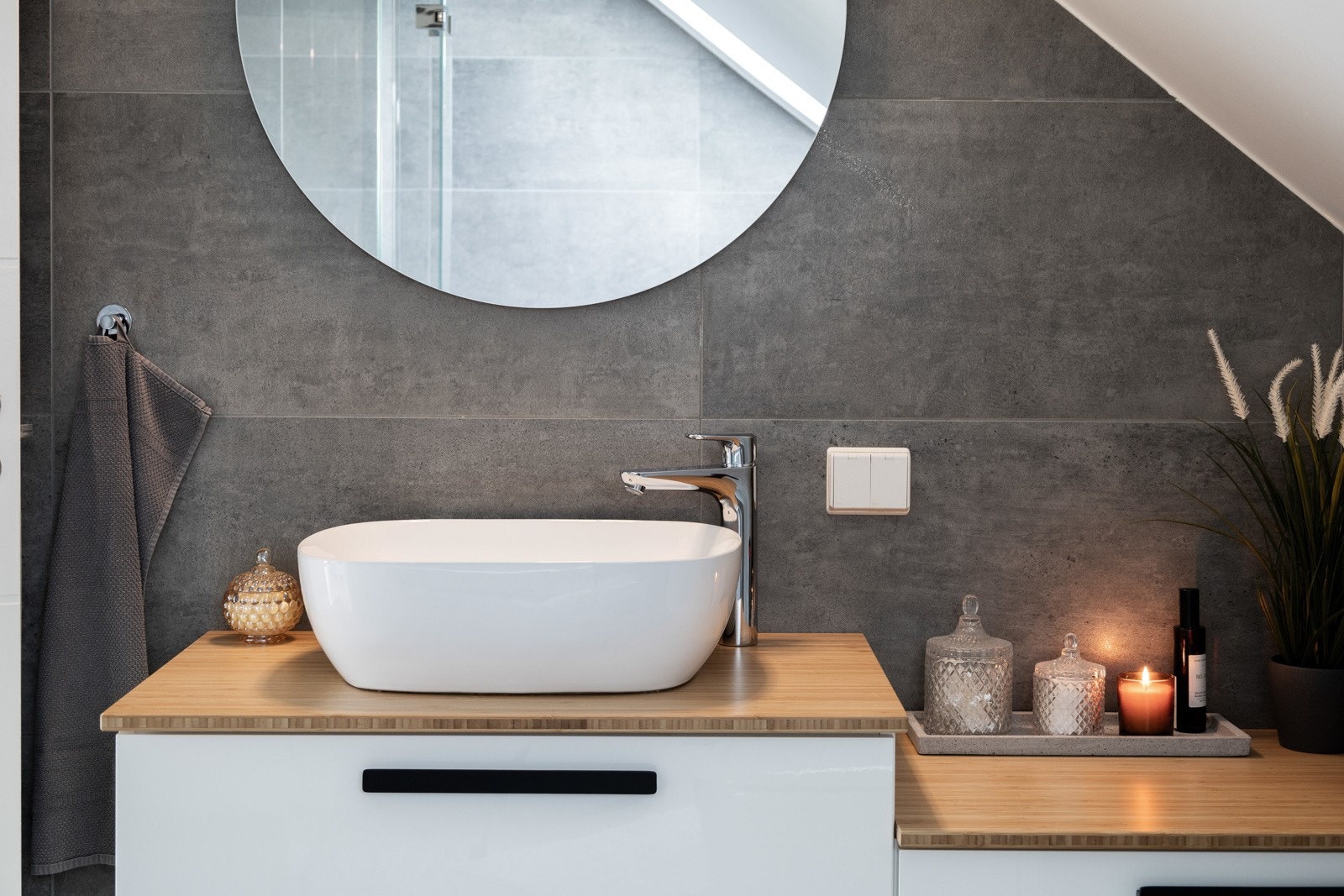 Moderne baderom med grå fliser, rund speil, servant på benkeplate og stilrent armatur. Galleribilde