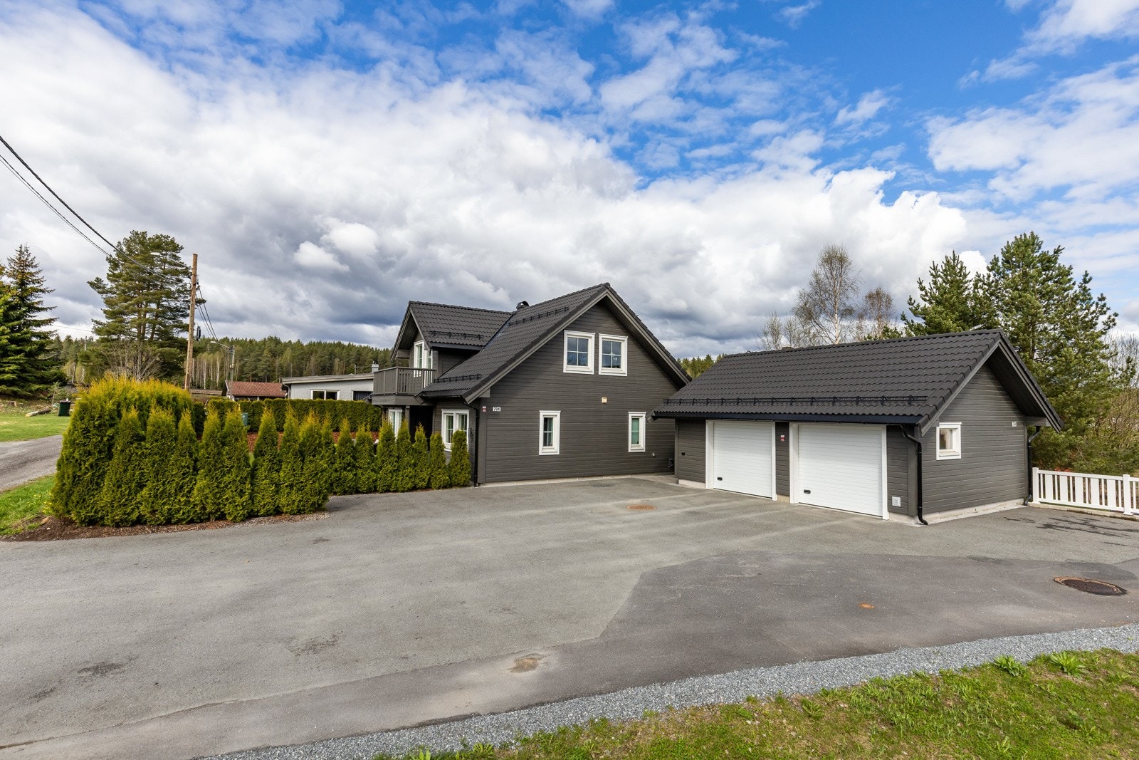 Enebolig med dobbelgarasje, asfaltert gårdsplass og omkranset av grønn hekk. Galleribilde