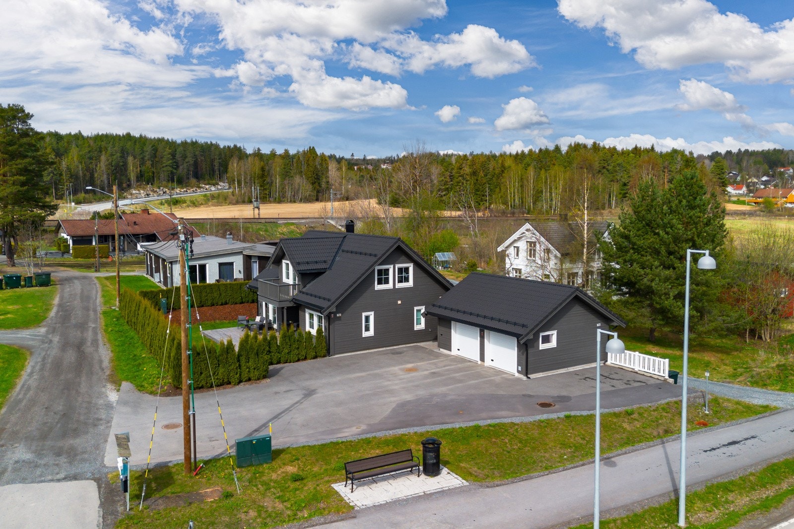 Enebolig med dobbel garasje og asfaltert gårdsplass, omgitt av grøntområder og skog i nærområdet. Galleribilde