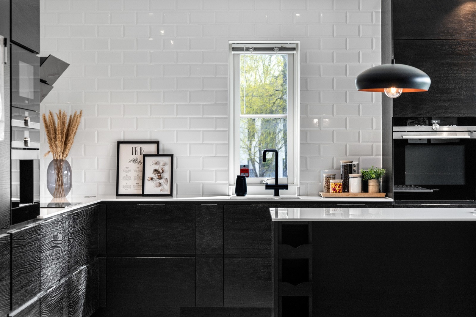 Moderne kjøkken med hvite fliser, svart innredning og en sentrert vindu som gir naturlig lys. Galleribilde