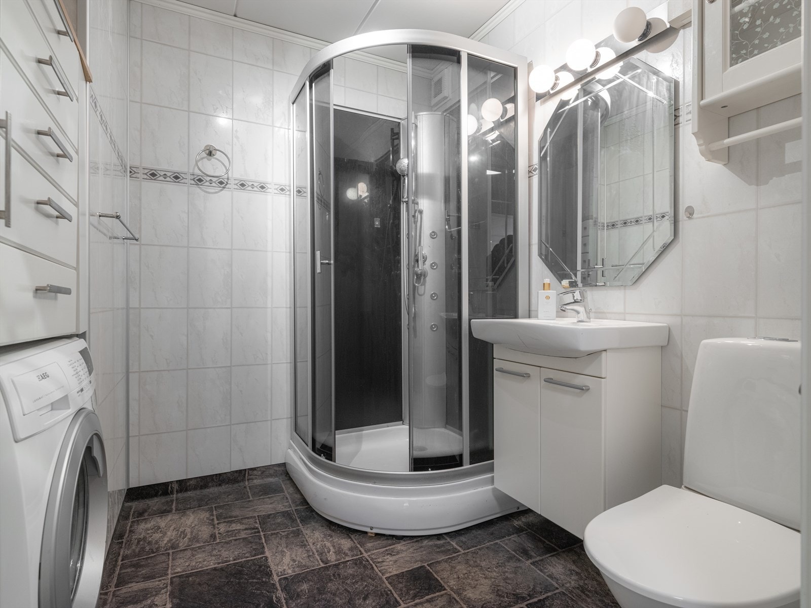 Badet er innredet med dusjkabinett, toalett, servantmøbel med underskap, speil og overlys. Det er opplegg for vaskemaskin. Galleribilde