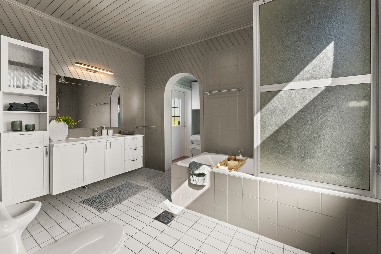 Badet i 1. etasje har god plass, og er innredet med stor baderomsinnredning med servant og høyskap, samt innfliset badekar, toalett og bidé Galleribilde