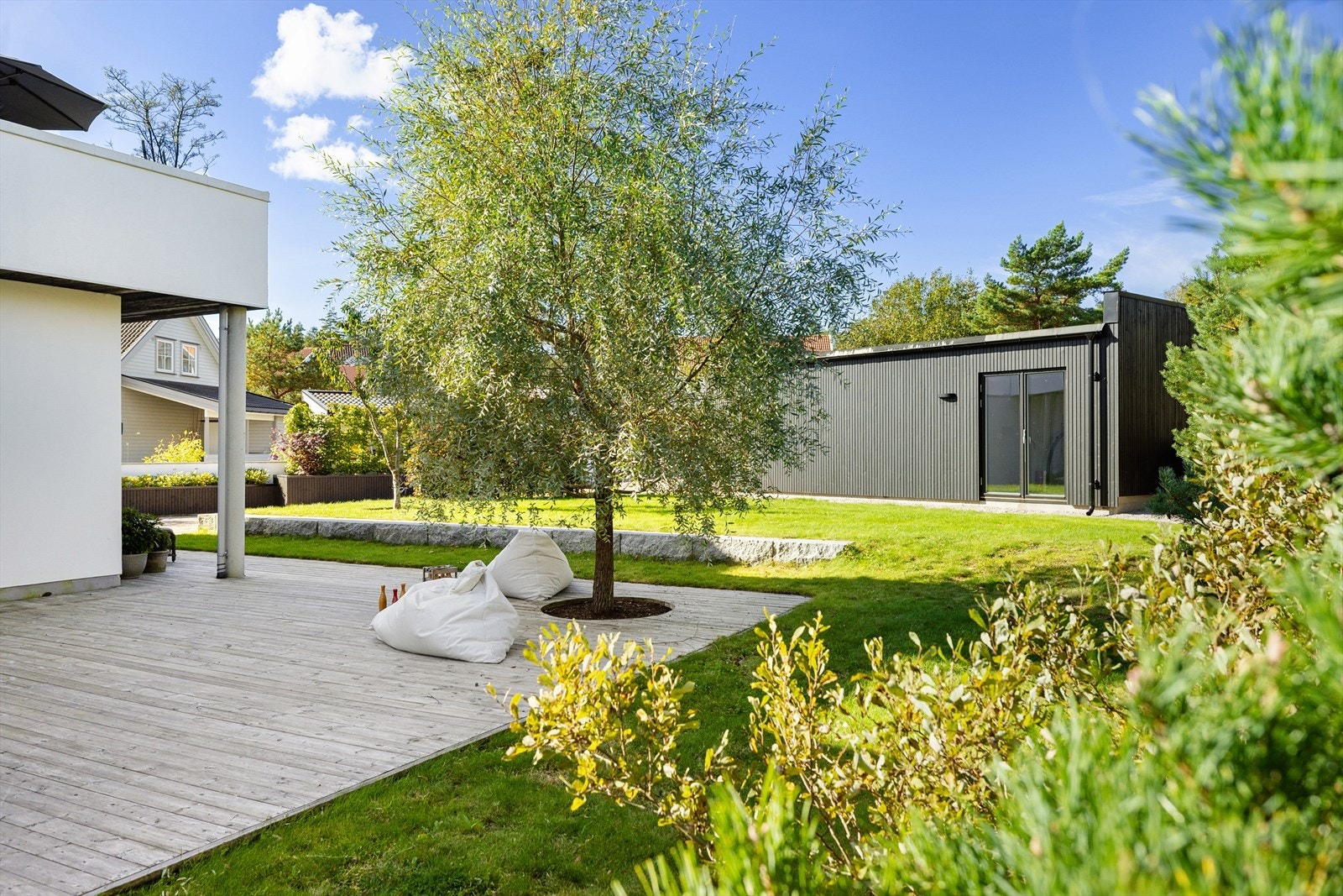 Hagen er ordnet og minimalistisk. Alt ligger i flukt; Den flate plenen glir sømløst over i terrassen, som glir sømløst inn i første etasje, og boligen reiser seg opp fra denne flaten, elegant og hvit. Galleribilde