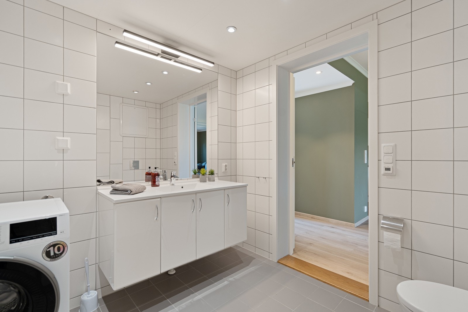 Badet er innredet med dusjsone, servant med skap, toalett og opplegg til vaskemaskin Galleribilde
