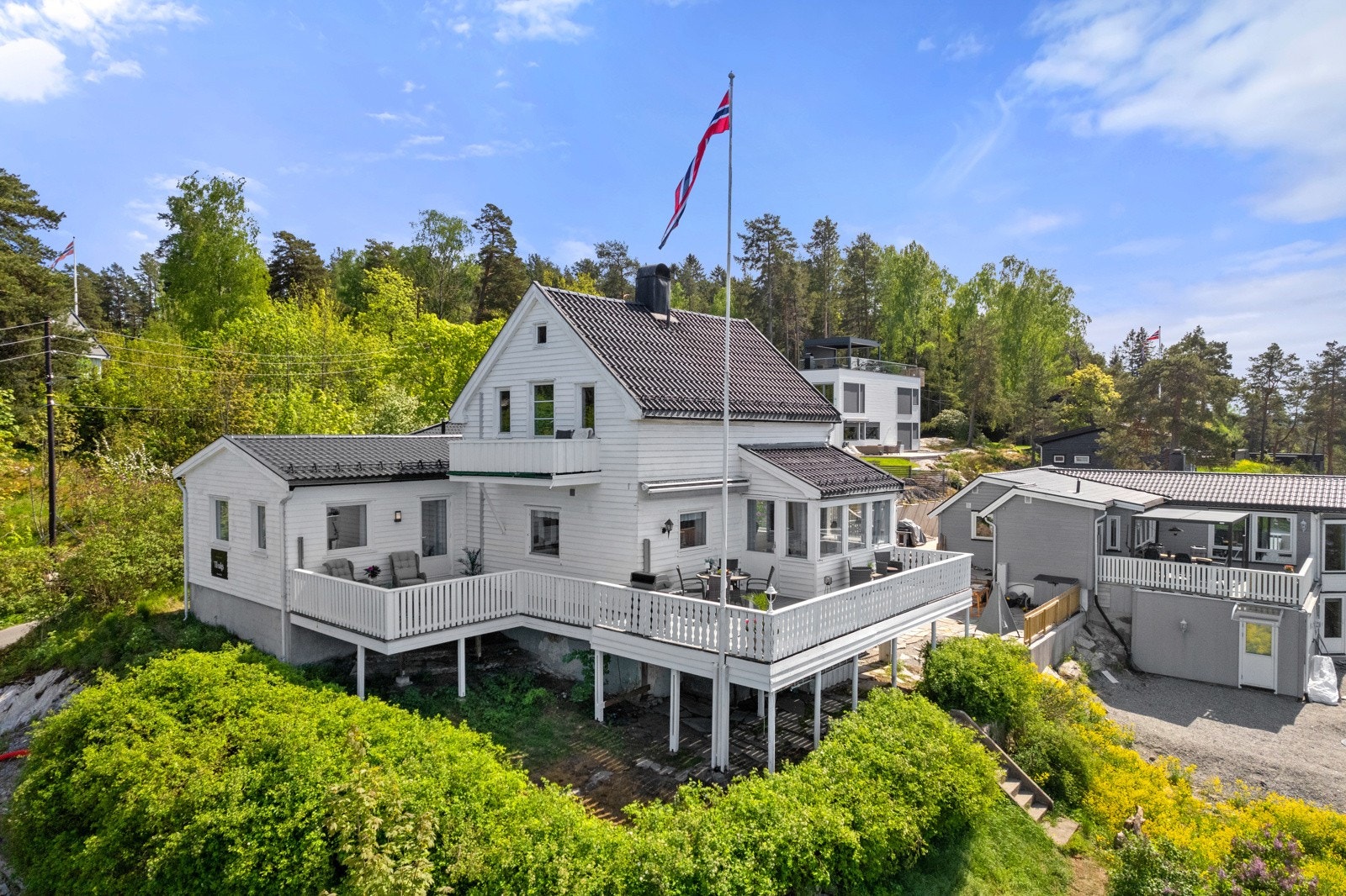 Boligen ligger høyt og solrikt plassert på tomten, omkranset av frodige busker på nedsiden. Galleribilde