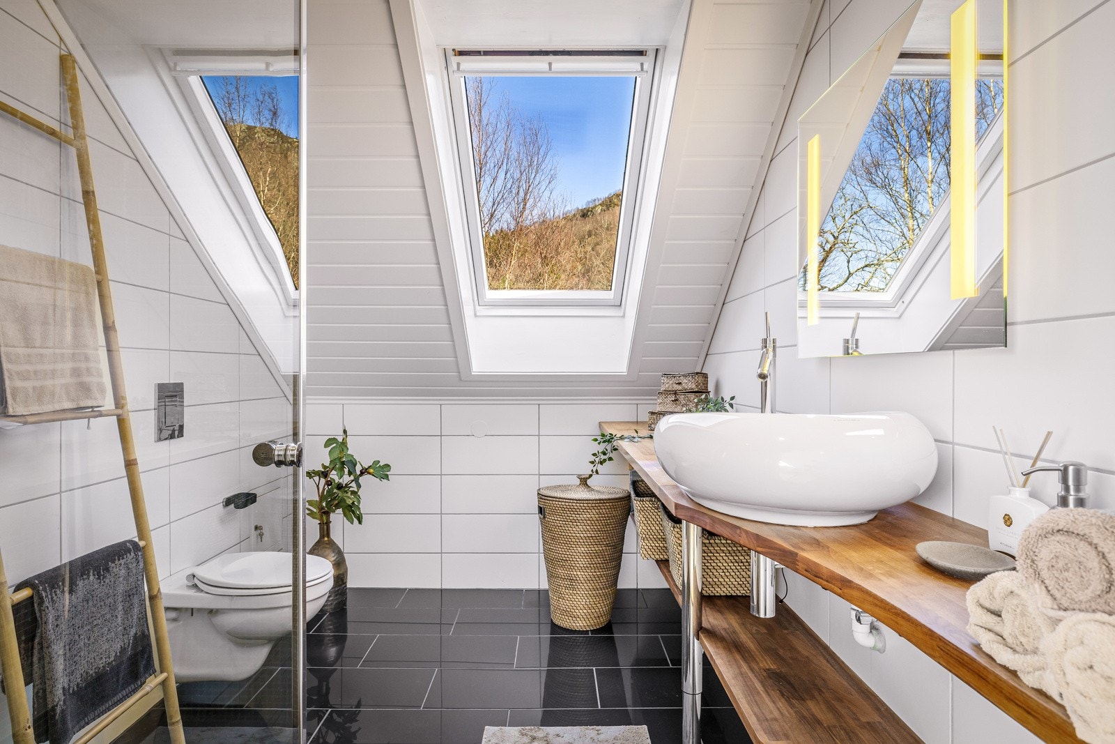 - Badet er innredet med vegghengt toalett, dusj med glass foldedør, servant med overhengende speil og belysning. Innredning i valnøtt er utført av snekker - Galleribilde