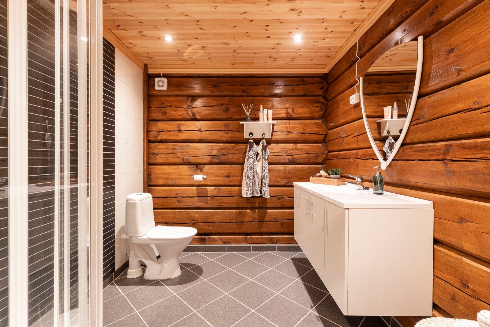 Badet har flislagt gulv, baderomspanel og tømmer på vegg Galleribilde