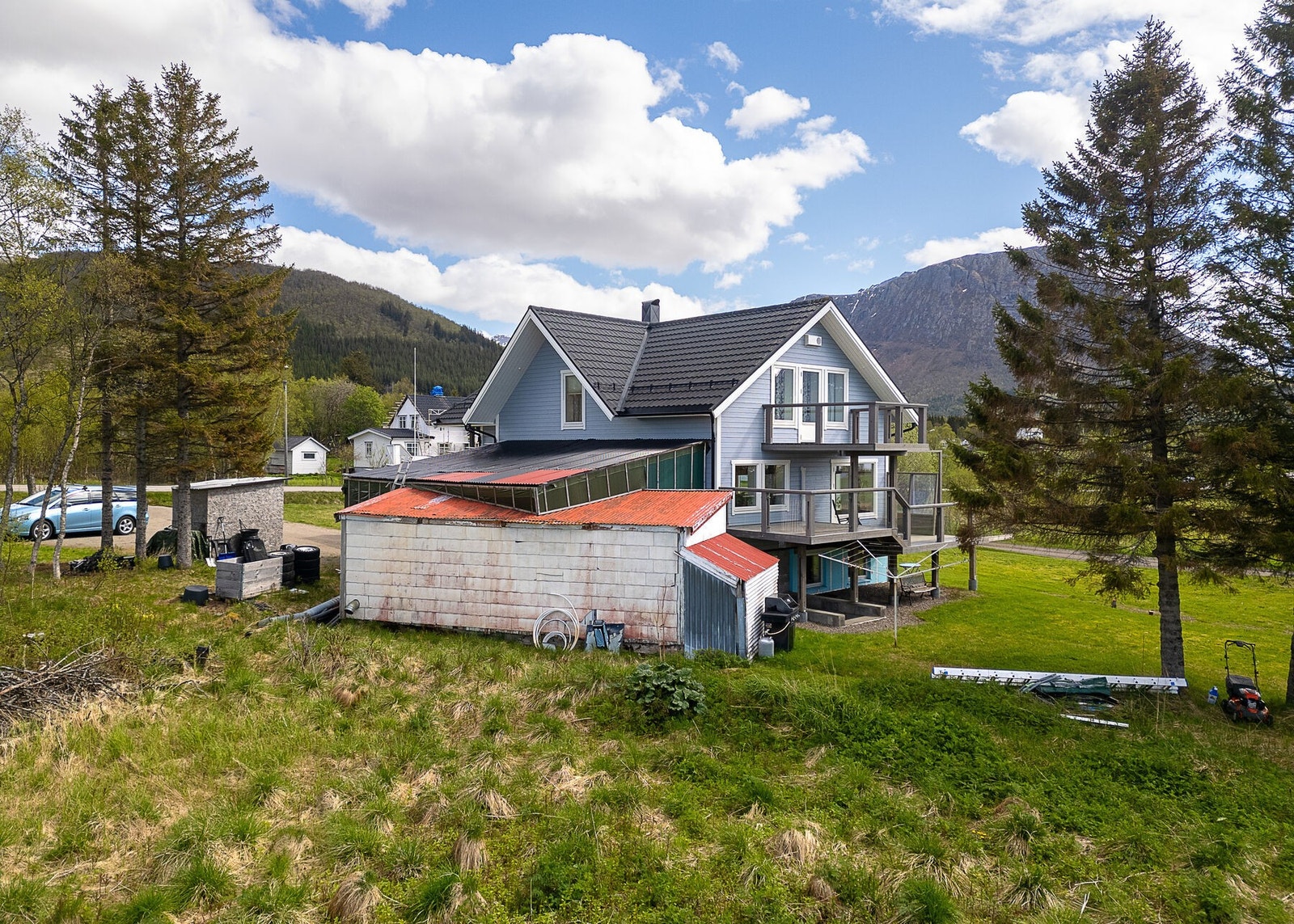 Fasade og uteområde. Stor opparbeidet tomt med plen, busker og trær. Parkering på gruslagt gårdsplass. Galleribilde