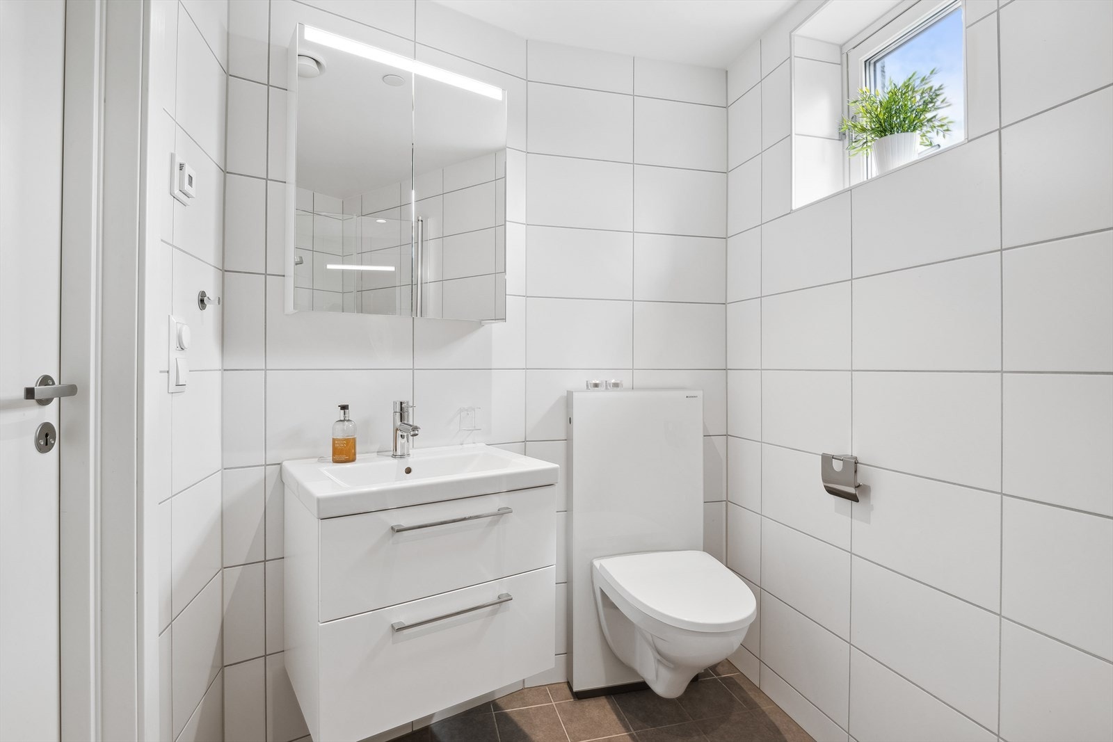 Badet er innredet med en praktisk og stilfull innredning med god oppbevaringsplass og servant, belyst speilskap for oppbevaring, elektrisk håndkletørker for den ekte hotellfølelsen i hverdagen og vegghengt toalett. Galleribilde